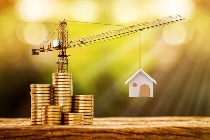 Coins and crane lifting up a tiny home is in reference to the construction loans in this article.