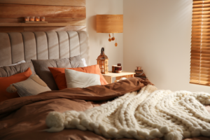 A fall décor bedroom with warm oranges and rusty colored bedding on bed and a chunky cream knit blanket.